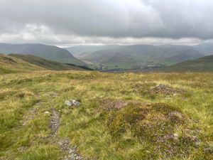 Looking over the edge of a rolling green hill into a small, distant village.