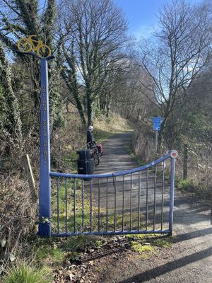 A threshold leading to a paved cycle path marked with a blue post for National Cycle Route 7. Jack waits with his bike a little ways down the path.