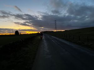 Night falling along quiet country roads, a small red light from the back of a bike is visible in middle distance