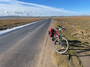 Red mountain bike with red bike bag on a causeway at low tide, sand rippling away from the paved road