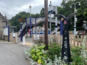 A charming blue and white railway station, with an arched bridge connecting the two platforms. A signpost at the gate for National Cycle Route 7 points to Glasgow in one direction and Inverness in the other.